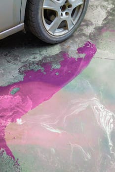 puddle of pink coolant and brown technical liquids on the concrete floor near car.