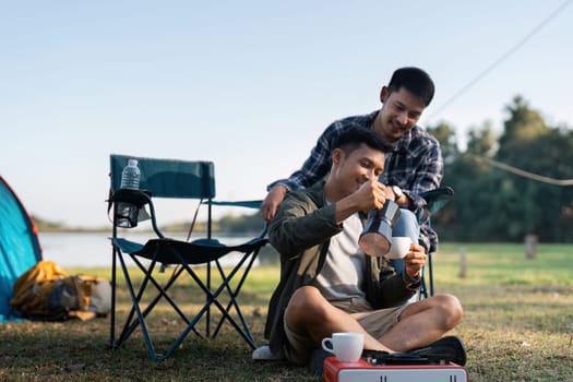 Gay LGBTQIA couple sitting on picnic chair drinking tea and coffee while camping on vacation holiday.