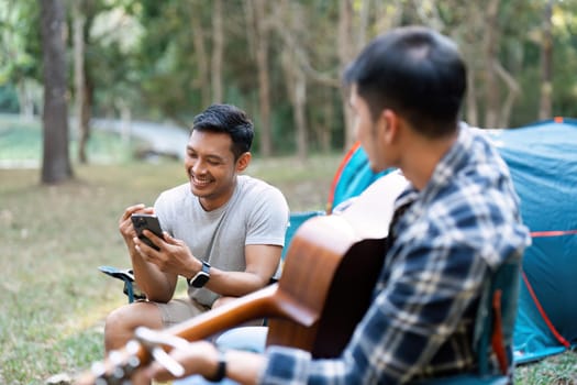 LGBTQIA Gay couple camping together in woods for holidays and relax on guitar together.