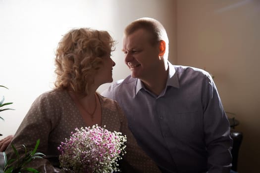 Loving adult couple communicates and embraces privately in the living room or in hotel. Woman is wearing business formal suit and man is wearing jeans and a shirt, indicating a close relationship