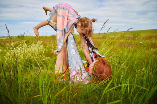 Happy female family with mother and daughter on green and yellow meadow full of grass and flower. Woman with red hair and blonde girl having fun, joy and hug in sunny summer day. Concept family love