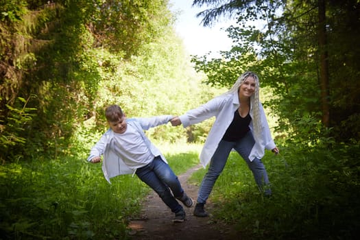 Funny mother with dreadlocks and fat boy happy walking in the forest on a sunny summer day