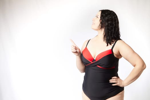 Portrait of attractive dreamy thick woman in red black swimsuit posing on white background. Body positive, photoshoot, selfie. Funny plus size model