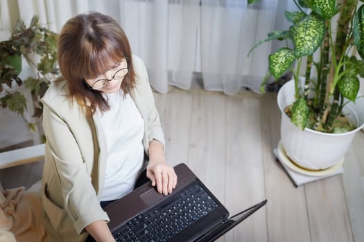 Elderly lady with glasses and laptop in room. Businesswoman is leader, manager working online. Blogger streaming. Grandma with family on Internet