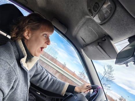 Terrified female driver a second before the accident. Scared middle-aged adult woman holds the steering wheel of car. Frightened Lady girl who is owner or rent a car for travel