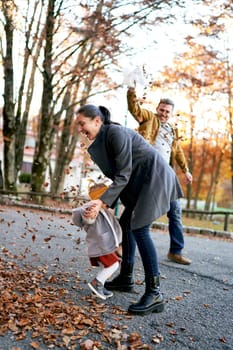 Mom and little girl dodge falling leaves from the bag in the hands of dad. High quality photo