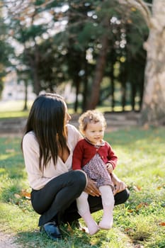 Little girl sits on her mother lap squatting in a sunny meadow. High quality photo