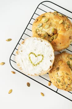 Freshly baked seed rolls on a cooling rack, one with a heart drawn in spices on cream cheese