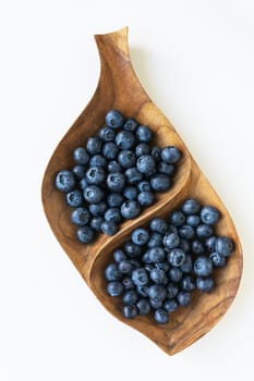 Leaf-shaped wooden bowl filled with fresh blueberries. Blueberries are ripe and have a bright dark blue color