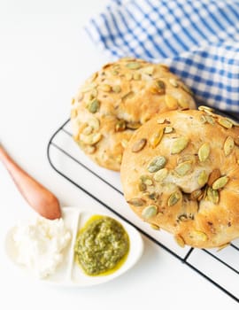 Fresh pumpkin seed bread with pesto and cream cheese on wire rack, blue checkered cloth background