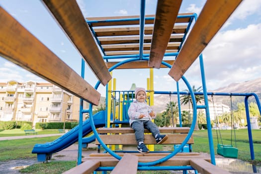 Little girl sits on a wooden bench with rings on the playground. High quality photo