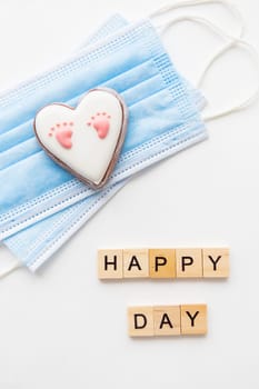 Disposable medical mask and two hearts. Heart with baby footprint. Childbirth in the coronavirus pandemic. Happy day lettering