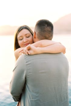 Woman with closed eyes hugs man neck on the seashore. High quality photo