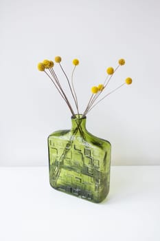 A green textured glass vase with yellow Craspedia flowers against a white background. Simple and elegant