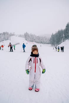 Little smiling girl stands on the ski slope against the backdrop of skiers. High quality photo