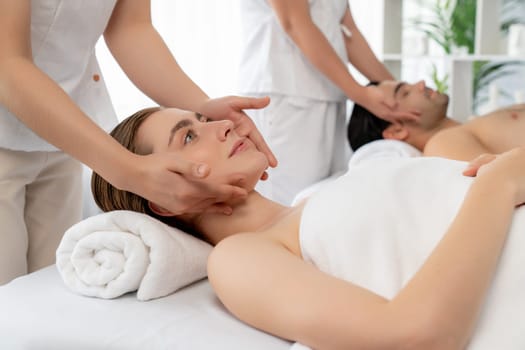 Caucasian couple enjoying relaxing anti-stress head massage and pampering facial beauty skin recreation leisure in dayspa modern light ambient at luxury resort or hotel spa salon. Quiescent