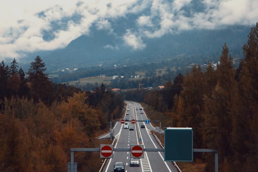 Autumn Voyage: A Highway Through Lush Fall Foliage with Mountains and Cloudy Skies in the Background. High quality photo