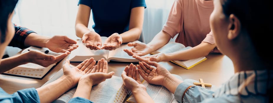 Cropped image of diversity people hand praying together at wooden church on bible book. Group of believer hold hand together faithfully. Concept of hope, religion, faith, god blessing. Burgeoning.