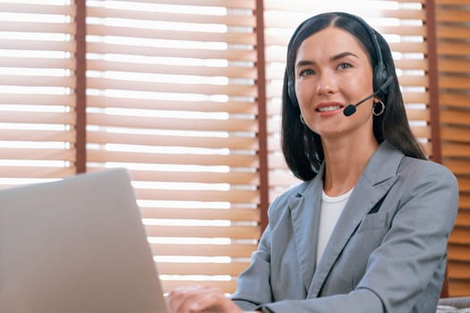 Female call center operator or customer service helpdesk staff working on workspace while talking on the headset to provide assistance for customer. Professional modern business service. Blithe