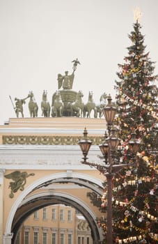 The main Christmas tree shimmers with lights of decorations through vintage lamppost, the central Palace square of the city decorated for the celebration during the snowfall, Arch of the General Staff. High quality photo