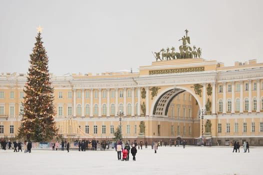 Russia, St. Petersburg, 30 December 2023: The main Christmas tree shimmers with lights of decorations on the central Palace square during the snowfall, Arch of the General Staff, a lot of people. High quality photo