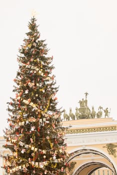 The main Christmas tree shimmers with lights of decorations, the central Palace square of the city decorated for the celebration during the snowfall, Arch of the General Staff, flag of Armed Forces. High quality photo