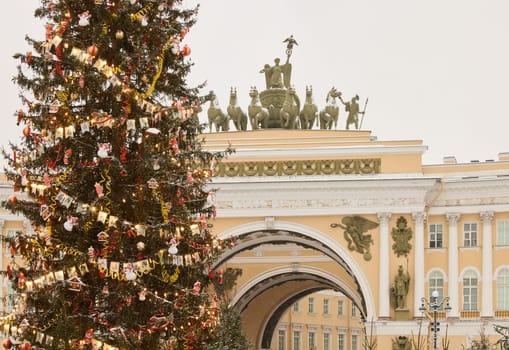 The main Christmas tree shimmers with lights of decorations, the central Palace square of the city decorated for the celebration during the snowfall, Arch of the General Staff, flag of Armed Forces. High quality photo