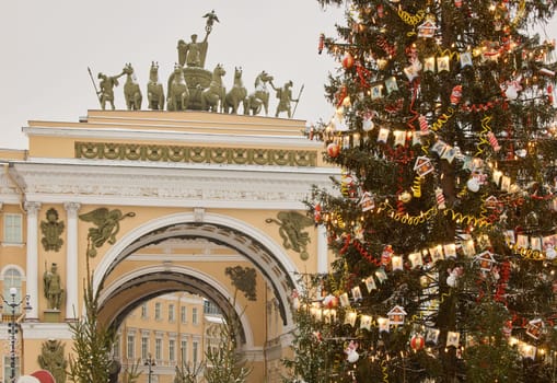 The main Christmas tree shimmers with lights of decorations, the central Palace square of the city decorated for the celebration during the snowfall, Arch of the General Staff, flag of Armed Forces. High quality photo