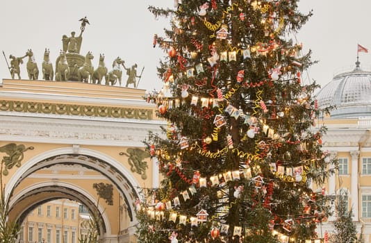 The main Christmas tree shimmers with lights of decorations, the central Palace square of the city decorated for the celebration during the snowfall, Arch of the General Staff, flag of Armed Forces. High quality photo