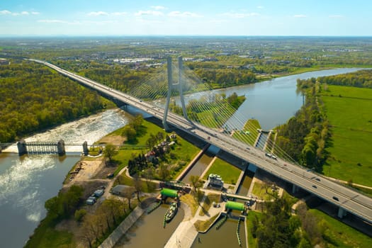 Vehicles drive on massive Redzinski Bridge in Poland on sunny spring day. Powerful cable-stayed pylon bridge built over Oder river aerial view