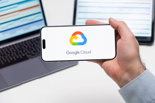 Google Cloud logo of app on the screen of mobile phone held by man in front of the laptop and tablet, December 2023, Prague, Czech Republic