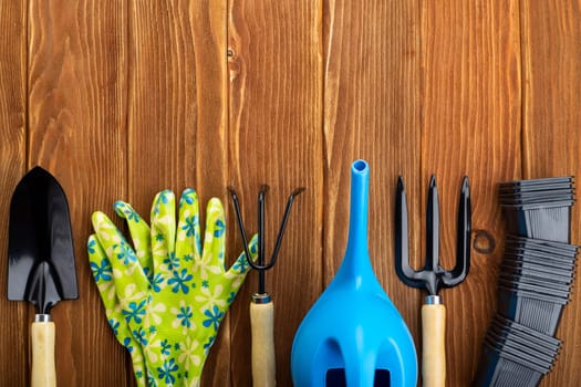 An assortment of essential gardening tools and bright floral gloves arranged neatly on a wooden surface, ready for garden maintenance.
