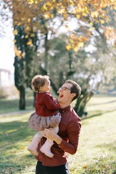 Laughing dad holding in his arms a laughing little girl in the park. High quality photo