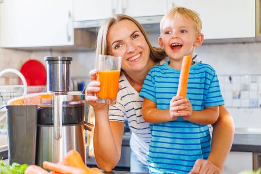 A joyful mother and her young son making healthy choices with fresh carrot juice in a bright kitchen, sharing a moment of happiness together.