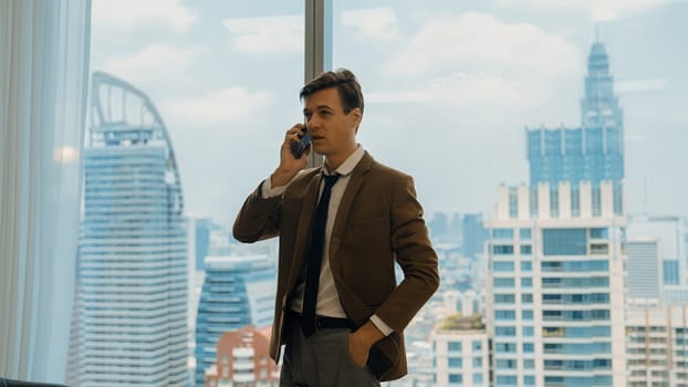 Businessman standing in ornamented office talking on phone with college on cityscape skyline window background. Determination and ambition drive business career toward to bright future