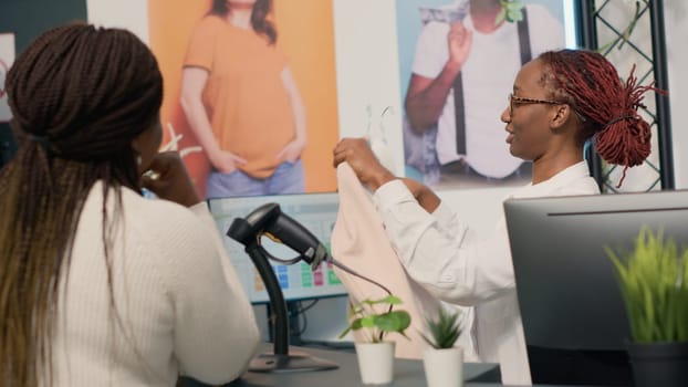 Woman on shopping spree in elegant clothing shop paying for clothes at checkout counter, helped by friendly worker. Shopkeeper assisting shopper with her purchases in fashion boutique