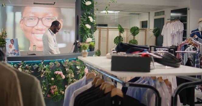 BIPOC man working in luxurious clothing store with elegant assortment of blazers. African american shopkeeper awaiting clients in premium fashion boutique with stylish attire garments