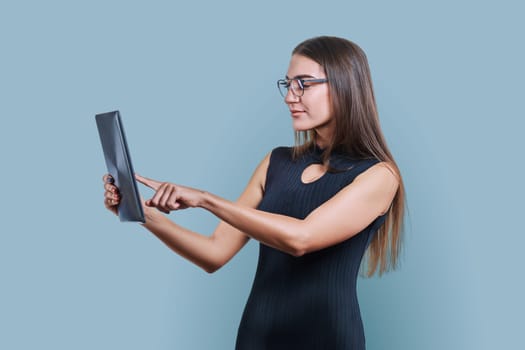 Young business woman with digital tablet on gray studio background. Fashionable elegant female in black dress looking at gadget screen. Technologies, business, work, job, executive, occupation