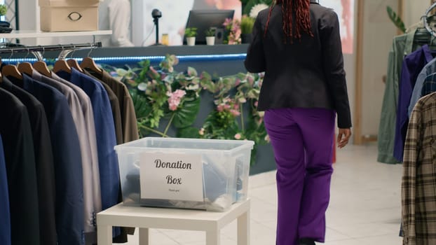 BIPOC shoppers in fancy fashion boutique donating their clothes for good cause. Customers placing garments in donation box, doing humanitarian gesture in premium clothing store