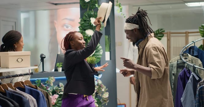 African american couple being silly together in clothing store, being happy about promotion sales. BIPOC clients in fashion boutique having fun, messing around, being excited about low prices