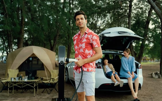 Outdoor adventure and family vacation camping in nature travel by eco friendly car for sustainable future. Lovely family recharge EV car with EV charging station in campsite. Perpetual