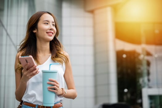 Modern woman in casual white shirt holding smartphone and water tumbler, staying hydrated on the go.