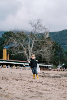 Little girl with a bag of trash stands looking around the beach. High quality photo