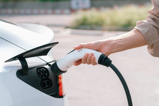 Closeup hand put EV charger to recharge electric car's battery from charging station in city commercial parking lot. Rechargeable EV car for sustainable environmental friendly urban travel. Expedient