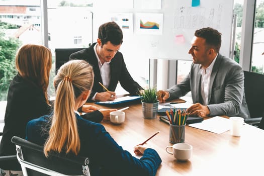 Businessman executive in group meeting discussion with other businessmen and businesswomen in modern office with coffee cups and documents on table. People corporate business working team concept. uds