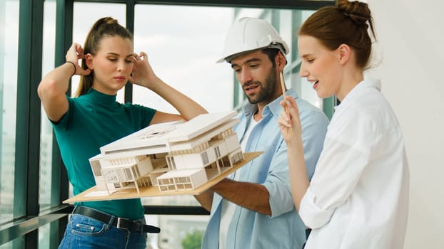 Skilled engineer holds house model and explain about house construction to skilled manager. Group of interior designer inspect architectural model. Working together, Civil engineering. Tracery