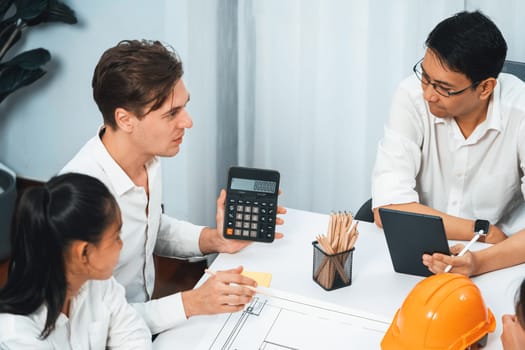 Diverse group of civil engineer and client working together on architectural project, building blueprint and calculate risk reduction for construction project at meeting table. Prudent