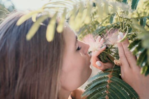 Beauty portrait of young woman closeup. Young girl smelling Chinese acacia pink blossoming flowers. Portrait of young woman in blooming spring, summer garden. Romantic vibe. Female and nature.