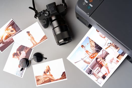 Photo camera with colorful printer photos on gray desk close up