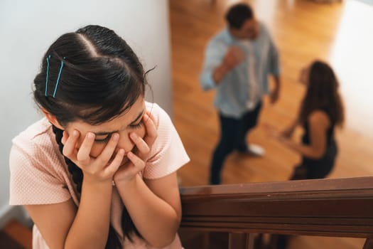 Stressed and unhappy young girl cover her ears blocking sound tension by her parent argument from the stair. Unhealthy family and domestic violence lead to traumatic childhood and anxiety. Synchronos